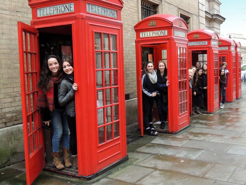 Group of teenage girls posing in red telephone booths in London.