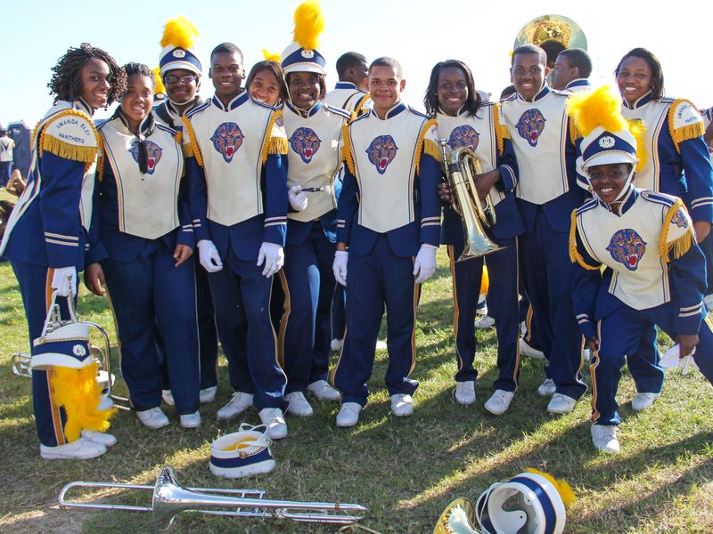 A high school marching band poses for a photo on a grassy field.