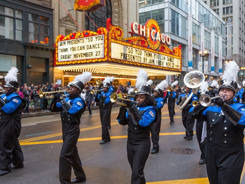 A marching band in blue and black uniforms with white plumes on their hats marches down a city street in Chicago, Illinois.