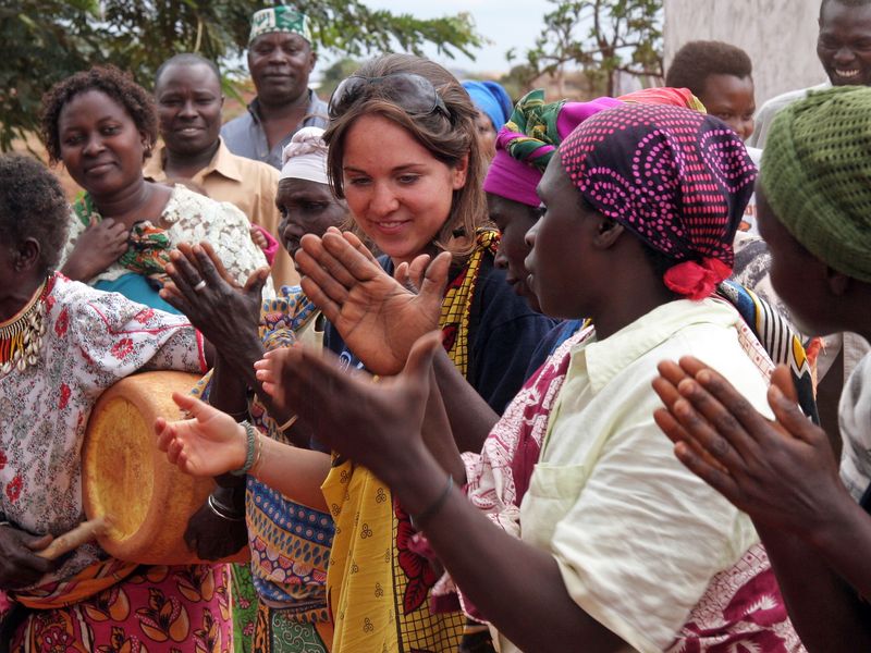 A group of African women and a young adult woman clapping and celebrating together.