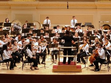 A youth orchestra performs on a grand stage in a beautiful concert hall.