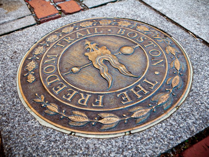 Close-up of a bronze Freedom Trail marker on a cobblestone street in Boston.