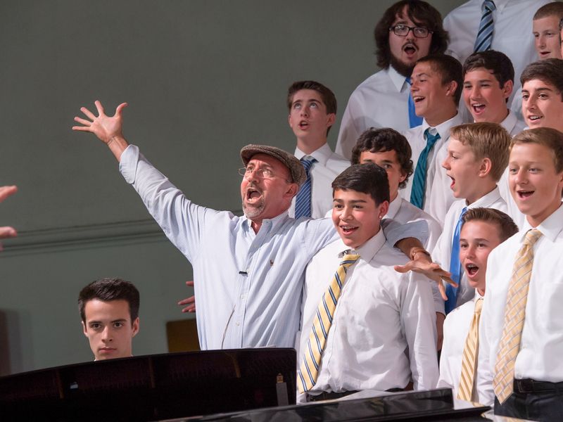 Choir director leading a group of teenage boys in song.