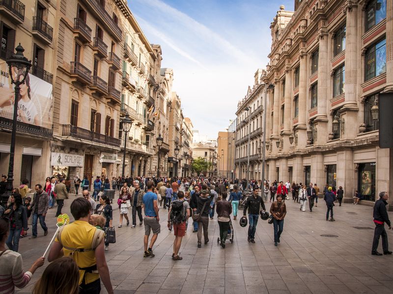 A vibrant street scene in Barcelona, Spain, filled with pedestrians of various ages enjoying the city's atmosphere and architecture.