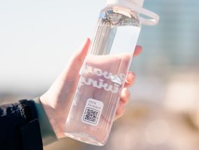 Hand holding a clear reusable water bottle with a QR code and "Fill it Forward" sticker, promoting sustainable hydration practices.