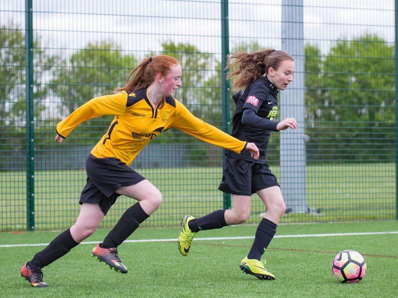 Two teenage girls playing a soccer game on a turf field.