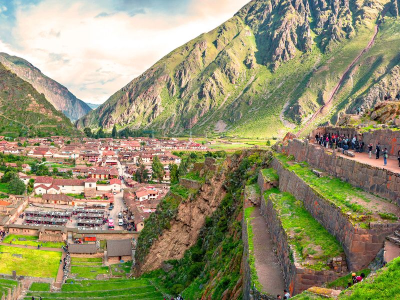 Panoramic view of Ollantaytambo ruins and town in the Sacred Valley of the Incas, Peru, showing agricultural terraces and tourists.