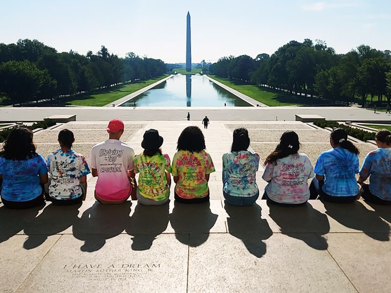 A group of teenagers at the Lincoln Memorial, facing the Washington Monument and Reflecting Pool.