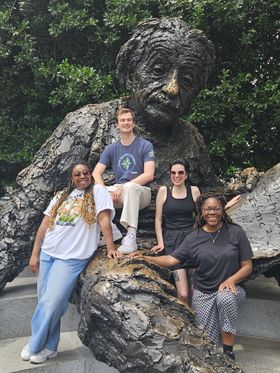 A group of four young adults posing for a photo with the Albert Einstein Memorial statue in Washington, D.C.