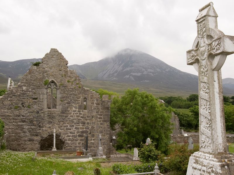 Historic cemetery with Celtic cross, church ruins, and mountain backdrop in Murrisk, County Mayo, Ireland