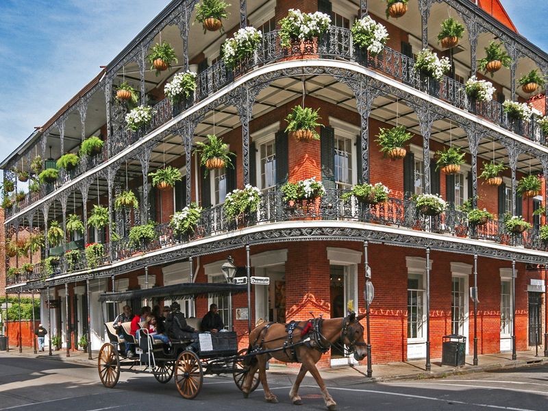 A horse-drawn carriage ride passes in front of a historic building with ornate ironwork balconies in the French Quarter of New Orleans.