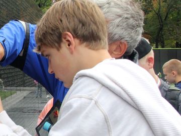 A teenager and an adult tracing a name on the Vietnam Veterans Memorial Wall.