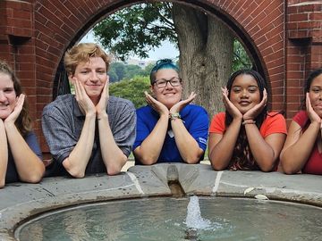 Six young adults playfully pose around a park fountain.