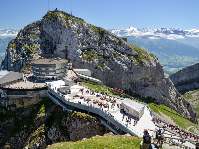 Pilatus Kulm: A panoramic view of the summit complex, with tourists enjoying the alpine scenery and a cogwheel train ascending the mountain.