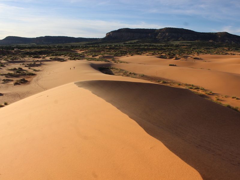 Three hikers enjoy traversing the vibrant orange Coral Pink Sand Dunes State Park in Utah.