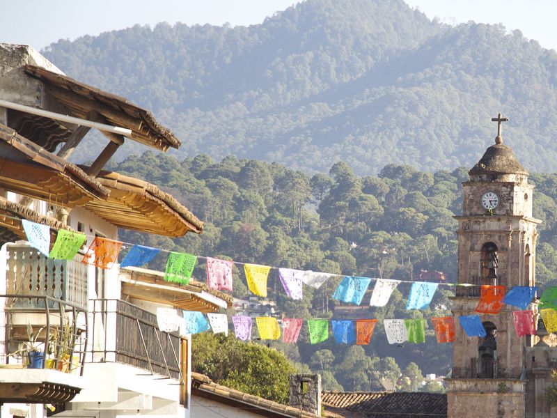 A vibrant Mexican town scene with colorful papel picado banners, a church, and a mountain backdrop.