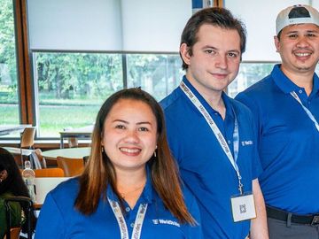 Group photo of eight individuals in blue polo shirts, representing teamwork and diversity in a casual indoor setting.