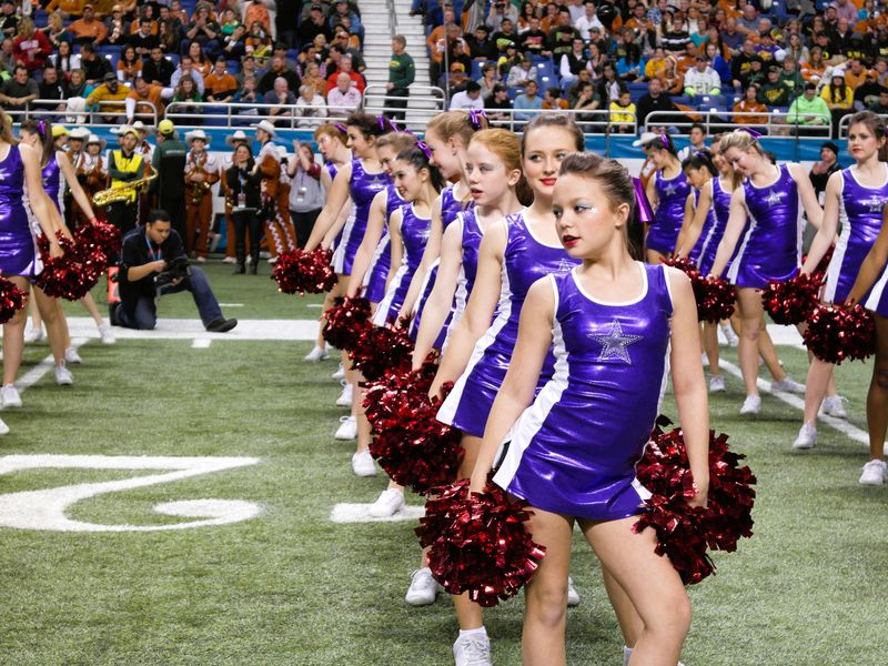 A line of cheerleaders performing on a football field.