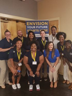 A group of young adults at a conference, posing for a photo in front of a banner that says 'Envision Your Future Starts Here.'