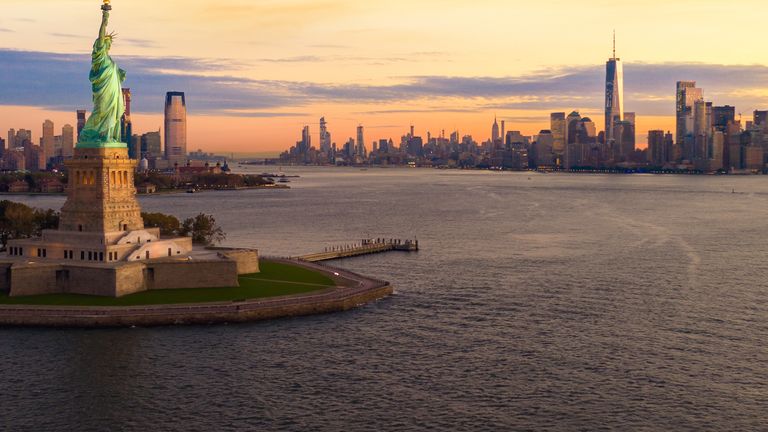 Aerial view of the Statue of Liberty at sunset with the New York City skyline in the background.