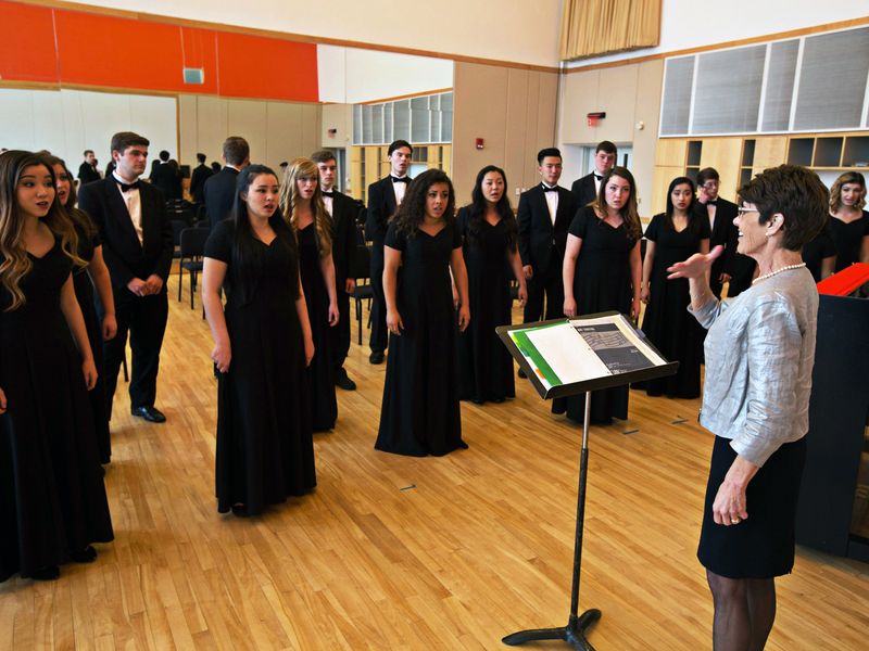 A high school choir receives instructions from their conductor during rehearsal.