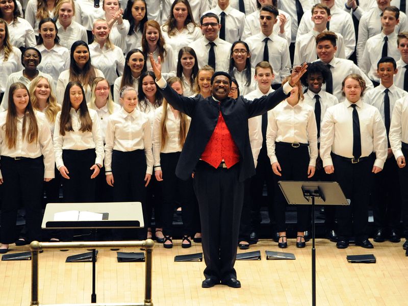 A conductor leads a choir of teenagers in a performance.