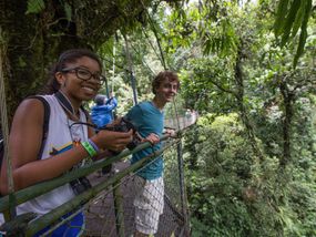 Two young adults standing on a hanging bridge in the rainforest.