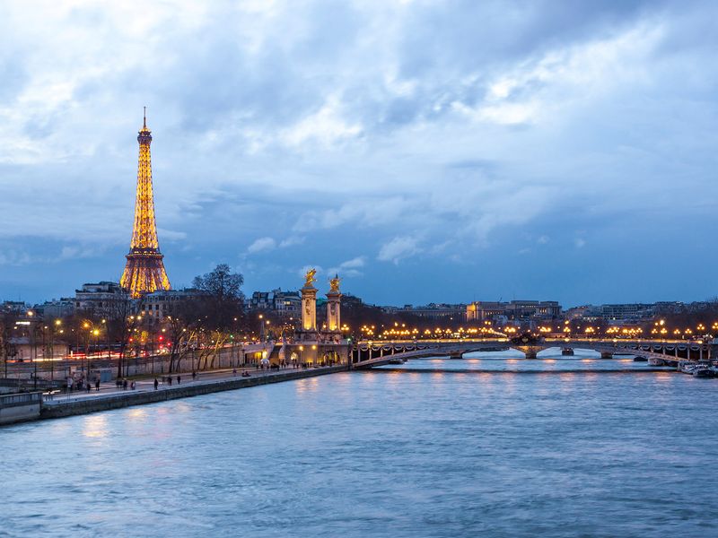 The Eiffel Tower and Alexandre III bridge illuminated at dusk in Paris, France.