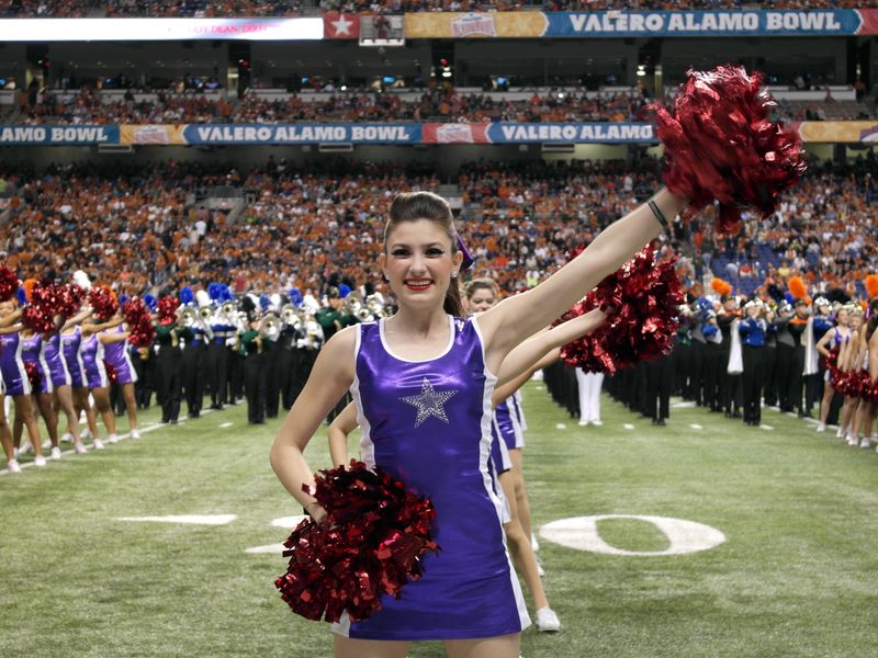 Cheerleader in purple uniform with red pom-poms performing on a football field