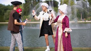 Young adults in historical costumes near a pond with fountains.