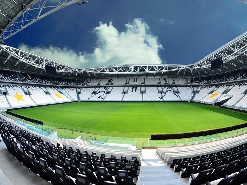 A wide-angle view of the Juventus Stadium in Turin, Italy, showcasing its modern architecture, lush green field, and black and white seating.