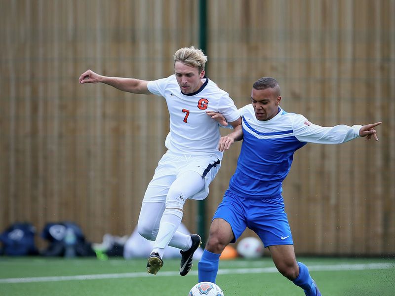 Two young adult men playing a game of soccer on a green field.