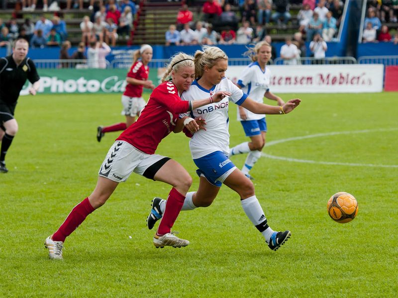 Two female soccer players competing for the ball during a game.