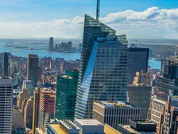 High-angle view of the New York City skyline on a sunny day, featuring the Empire State Building and other skyscrapers.