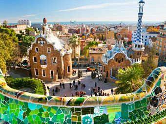 Tourists gather in Park Güell in Barcelona, Spain, admiring the colorful architecture and city views.