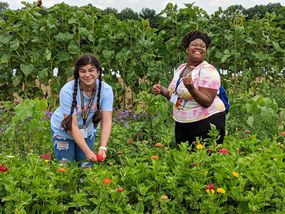 Two teenage girls, enjoying the summer weather in a garden filled with flowers.