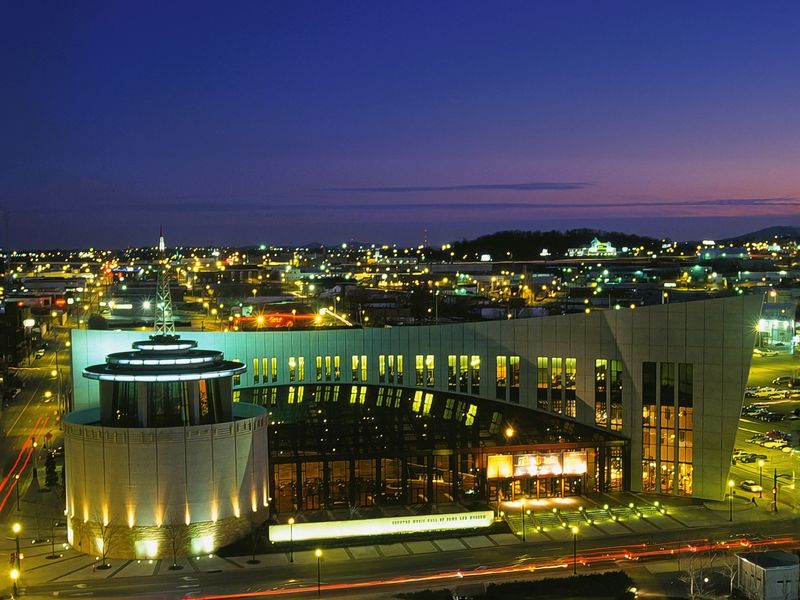 A night view of Nashville, Tennessee featuring the illuminated Country Music Hall of Fame and Museum. Long exposure of the cityscape creates light trails from passing cars. 