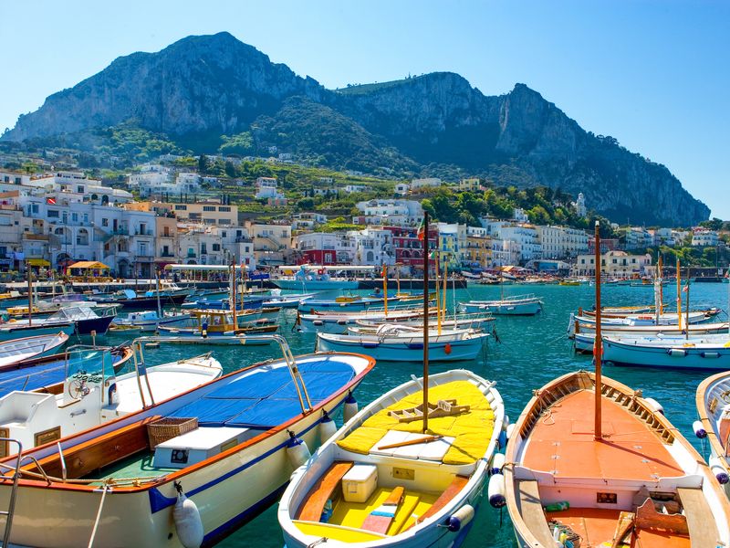 Colorful rowboats in Capri harbor, with town and cliffs in background.