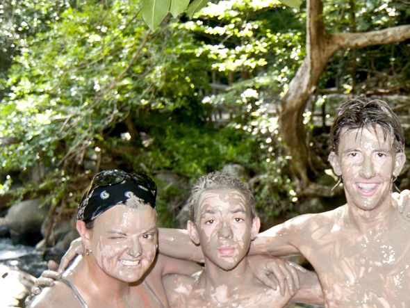 Five friends covered in mud smiling for a photo in the forest.