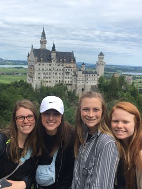 Four young adults take a selfie with the majestic Neuschwanstein Castle in the backdrop.