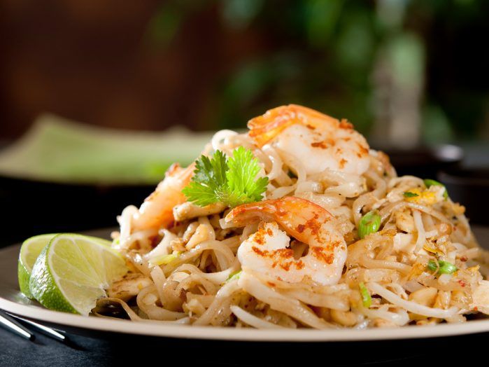 A plate of Pad Thai garnished with shrimp, cilantro, and lime wedges.