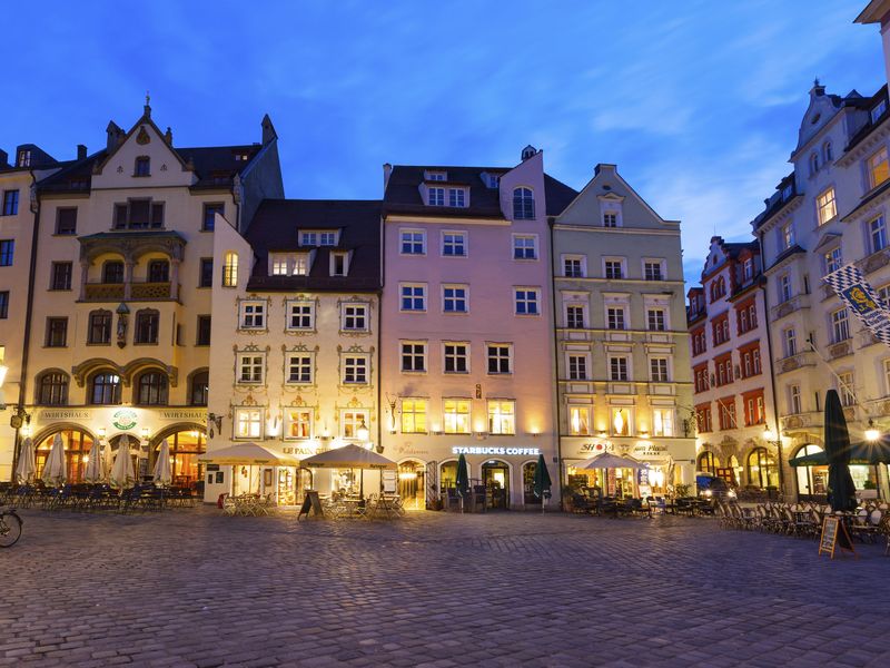 Cobblestone plaza in Augsburg, Germany at dusk, with colorful buildings, cafes, and a Starbucks.