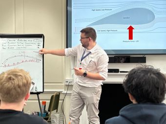 A teacher explaining the principles of aerodynamic lift to a group of students using a whiteboard and a projected diagram.