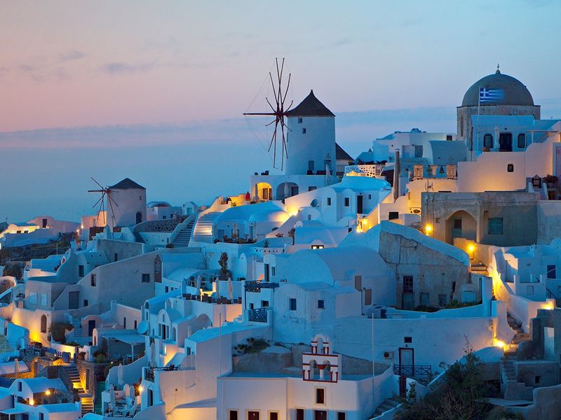 White-painted buildings and windmills on a hillside in Oia, Santorini, Greece during a beautiful sunset.