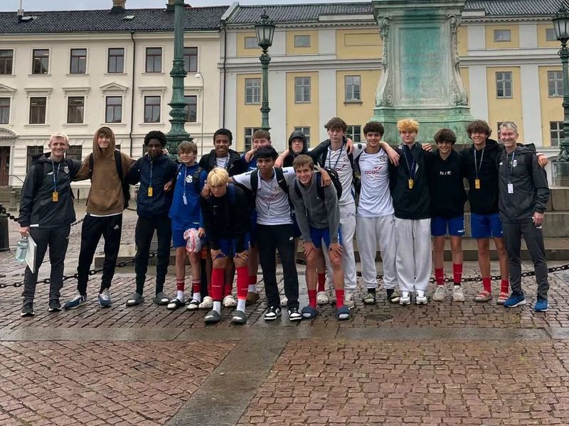 Group photo of a teenage soccer team and coach in a city square in Europe.