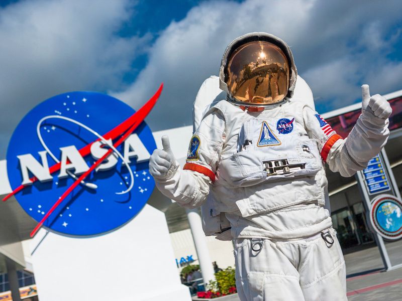 Astronaut giving a thumbs up in front of the NASA logo.