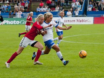 Two female soccer players competing for the ball during a game.