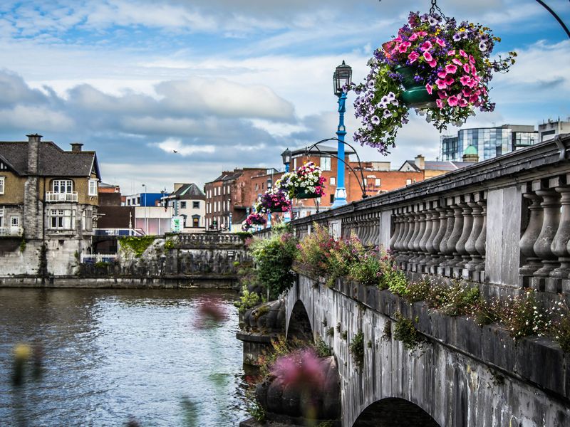 A stone bridge with colorful flower baskets overlooking a river in Ireland.