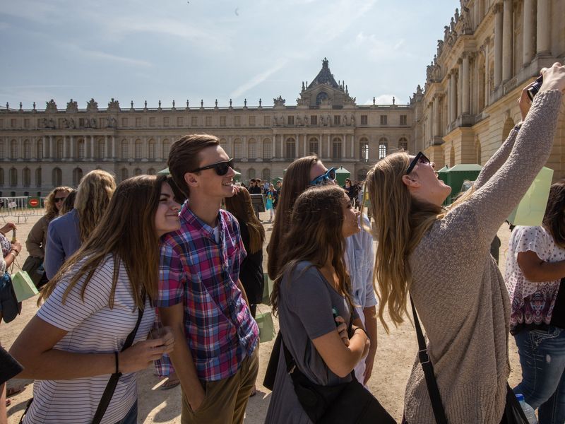 A group of friends takes a selfie in front of the Palace of Versailles.