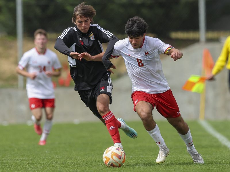 Two young adult soccer players compete for the ball during an intense game. One player wears a white and red uniform, and the other wears a black and white uniform. The motion is evident in their dynamic poses, capturing the fast-paced nature of the sport. 